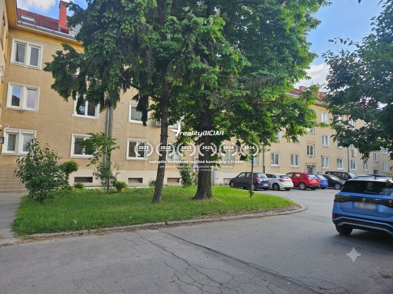 Kompletne zrekonštruovaný 3-izbový byt na Študentskej ulici v Trnave - Parkovisko pri 3-izbových bytoch na Študentskej ulici v Trnave, obklopené zeleňou a stromami.