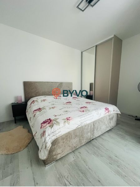 Na predaj 2.izbový byt v staršej novostavbe na začiatku Petržalky - Spálňa v 2-izbovom byte s posteľou a skriňou, svetlé steny, podlaha s dreveným dekorom.