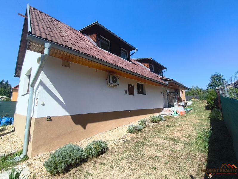 S láskou budovaný domov s dušou v Divín – opäť voľný - Rodinný dom v Divíne s hnedou strechou a záhradou, lemovaný trávnikom a kríkmi.