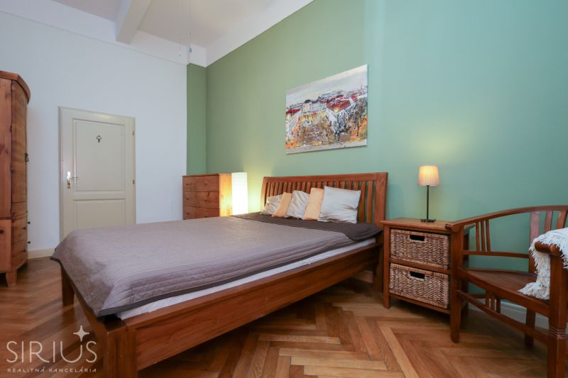 LAURINSKÁ, 2i byt, 68m² – REPREZENTATÍVNE bývanie v historickom CENTRE - Spálňa v 2-izbovom byte s posteľou, kreslom a podlahou s dreveným dekorom.