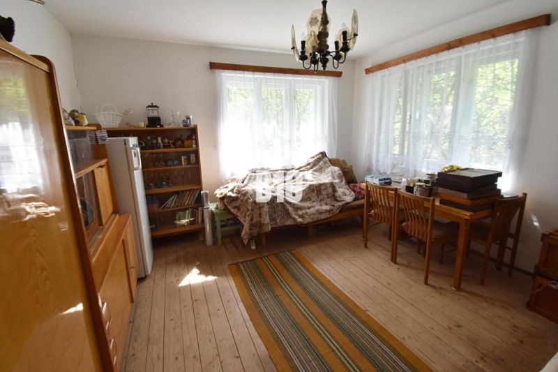 Rodinný dom v pôvodnom stave -Dlhé Pole - Obývačka v rodinnom dome s podlahou s dreveným dekorom, sedačkou a stolom.