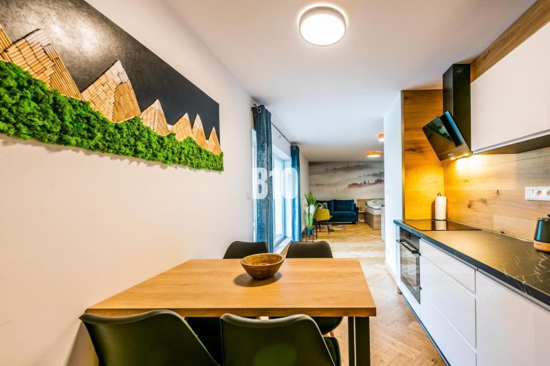 Investičný APARTMÁN v centre Terchovej - Interiér rekreačného apartmánu s kuchynskou linkou a stolom, podlaha s dreveným dekorom.
