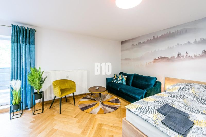 Investičný APARTMÁN v centre Terchovej - Štýlový rekreačný apartmán s podlahou s dreveným dekorom, pohovkou a rastlinami.