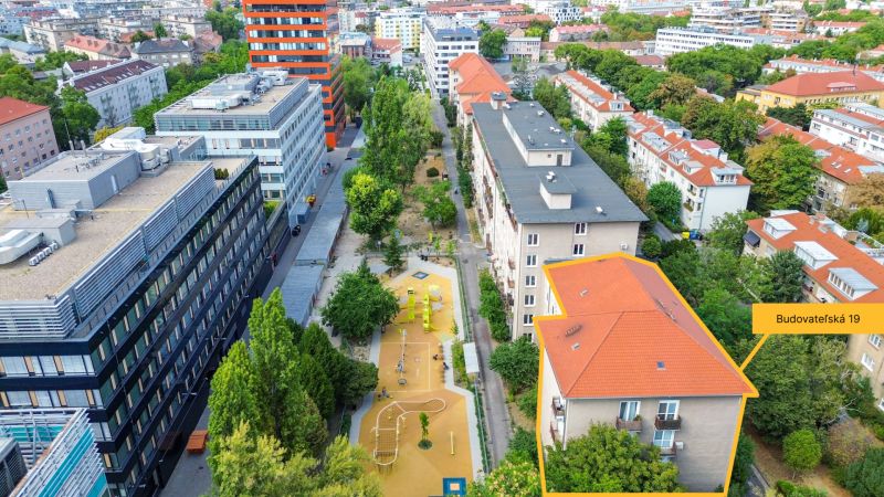Priestranný 2i byt v obklopení zelene len pár krokov od OC Nivy | 53m² - Letecký pohľad na Budovateľskú ulicu v Bratislave - Ružinove s bytovými domami a ihriskom.