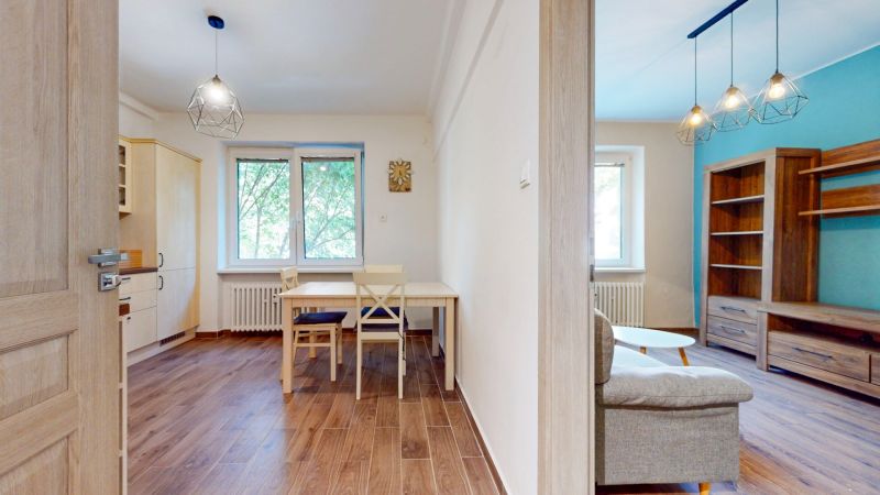 Priestranný 2i byt v obklopení zelene len pár krokov od OC Nivy | 53m² - Kuchyňa s jedálenským stolom a obývačka s podlahou s dreveným dekorom v 2-izbovom byte.