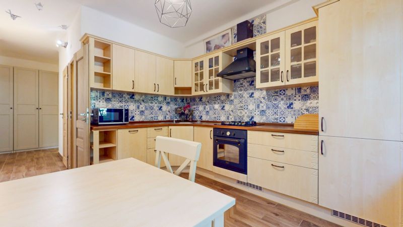 Priestranný 2i byt v obklopení zelene len pár krokov od OC Nivy | 53m² - Kuchyňa v 2-izbovom byte s drevenými skrinkami, modrými obkladmi a podlahou s dreveným dekorom.