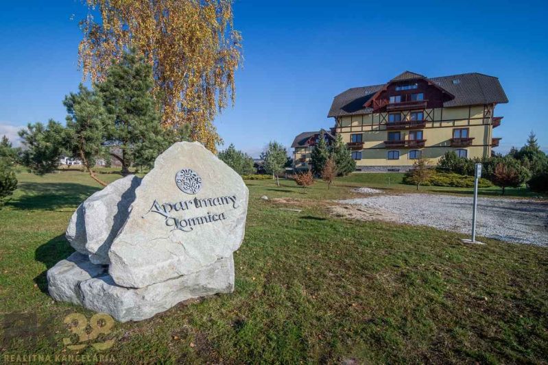 Na predaj: 2-izbový byt s garážou pod Vysokými Tatrami  - Apartmánový komplex vo Veľkej Lomnici, na trávnatej ploche s veľkým kamenným nápisom.