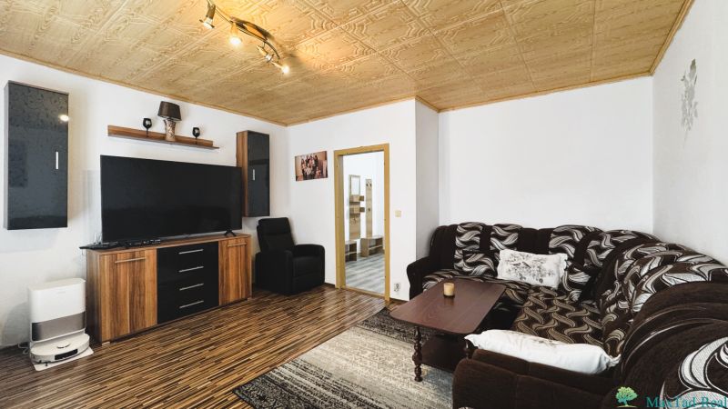 94,66 m², štyri izby a nikto nad hlavou. A Komenského má svoje výhody! - Obývacia izba so sedacou súpravou a podlahou s dreveným dekorom v 4-izbovom byte.