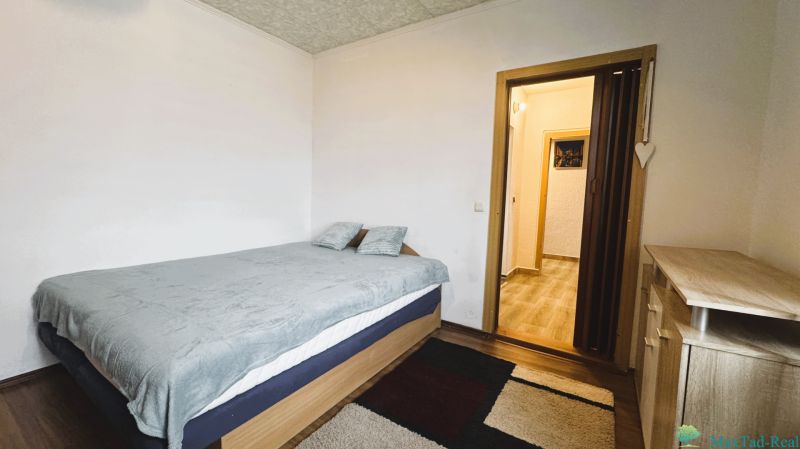 94,66 m², štyri izby a nikto nad hlavou. A Komenského má svoje výhody! - Spálňa v 4-izbovom byte s postelou, kobercom a nábytkom s dreveným dekorom.