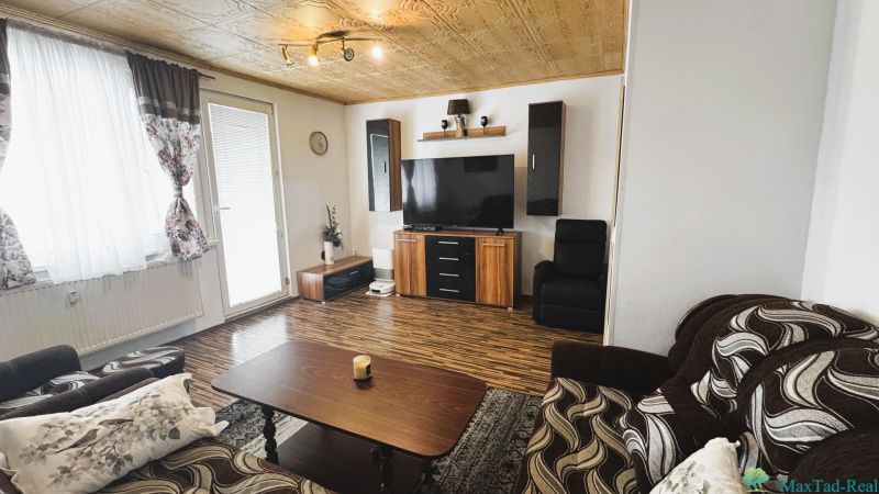 94,66 m², štyri izby a nikto nad hlavou. A Komenského má svoje výhody! - Obývacia izba v 4-izbovom byte s podlahou s dreveným dekorom a televízorom na stene.