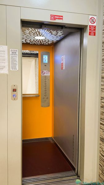 94,66 m², štyri izby a nikto nad hlavou. A Komenského má svoje výhody! - Otvorený výťah v budove 4-izbového bytu s oranžovým interiérom.