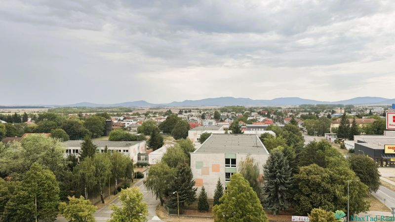 94,66 m², štyri izby a nikto nad hlavou. A Komenského má svoje výhody! - Pohľad na Komenského ulicu v Trebišove s budovami a zeleňou.