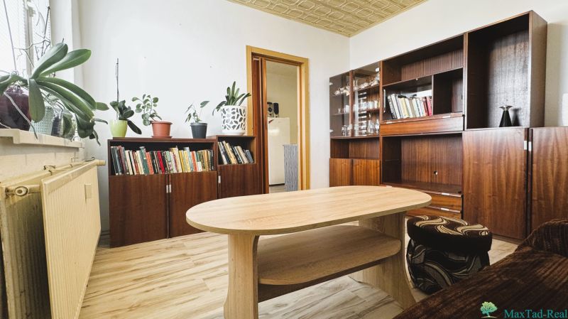 94,66 m², štyri izby a nikto nad hlavou. A Komenského má svoje výhody! - Obývačka so skriňami, knihami, kvetmi a podlahou s dreveným dekorom v 4-izbovom byte.