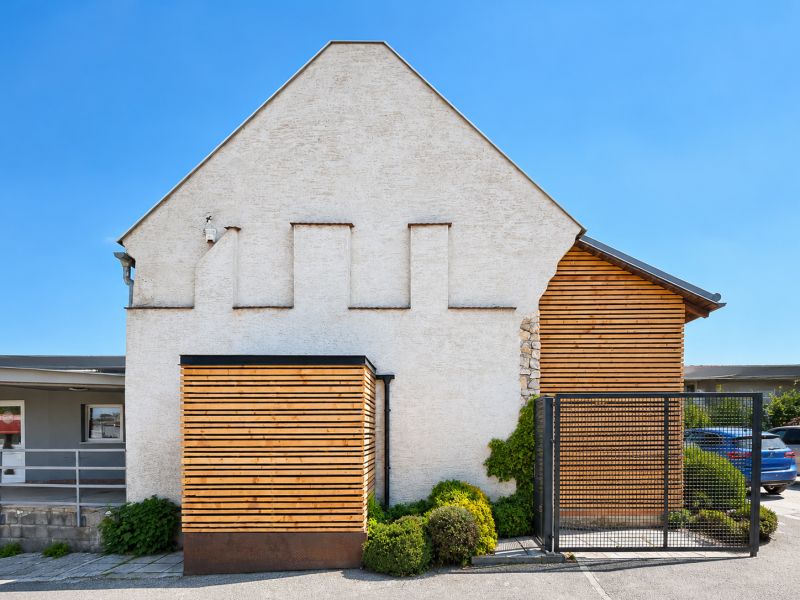 Multifunkčný dom 156 m² | bývanie, podnikanie, Trstín - Budova v Trstíne s drevenými a kamennými prvkami, vedľa parkoviska.