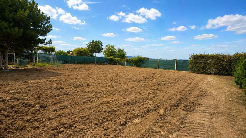 NA PREDAJ – rovinatý stavebný pozemok v Pravoticiach | 660 m² - Pozemky na bývanie v Pravoticiach s obrábanou pôdou, zeleným plotom a modrou oblohou.