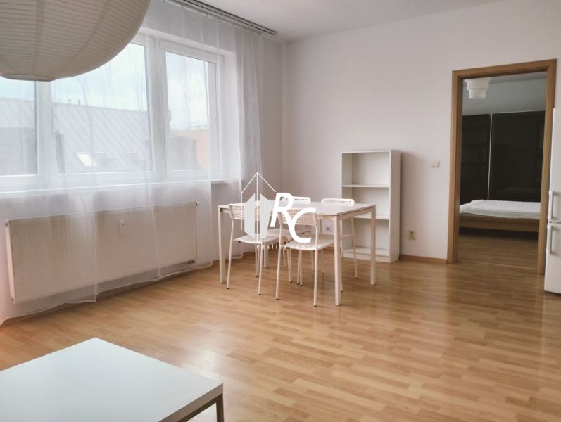 Prenájom dvoch 2-izbových bytov vedľa seba, Martin - centrum - 2-izbový byt s podlahou s dreveným dekorom, biely stôl s priehľadnými závesmi.