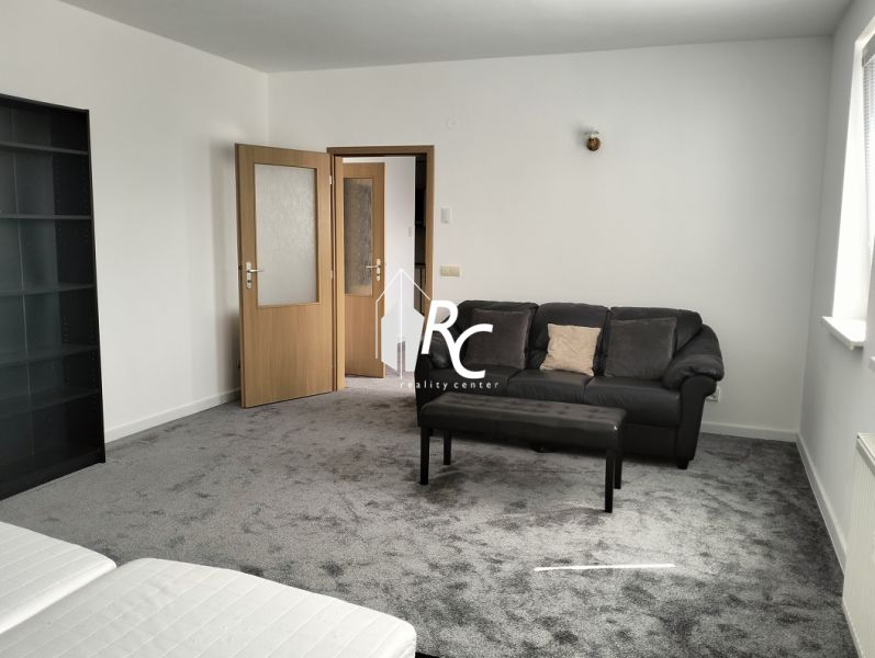 Prenájom dvoch 2-izbových bytov vedľa seba, Martin - centrum - Obývacia izba v 2-izbovom byte s tmavým kobercom, pohovkou a kreslom.