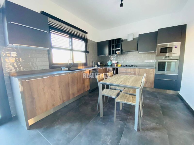 MODERNÁ VILA 3+1 S VÝHĽADOM NA MORE A HORY | YENİ BOĞAZİÇİ, - Kuchyňa s dreveným dekorom, moderné spotrebiče, priestranný stôl a sivé skrinky.