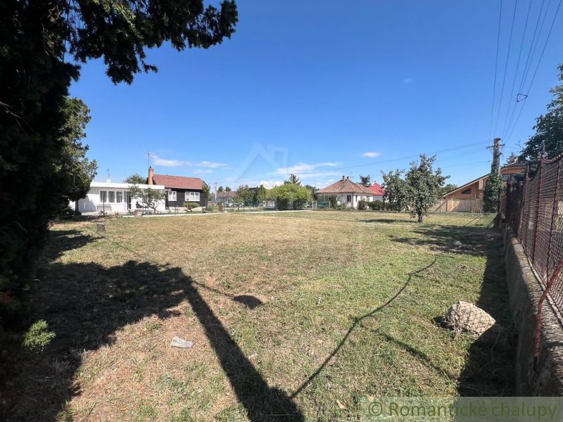 Veľký pozemok na výstavbu v centre Bernolákova. - Záhrady v Bernolákove s trávnikom, stromami a okolostojacimi domami za slnečného dňa.