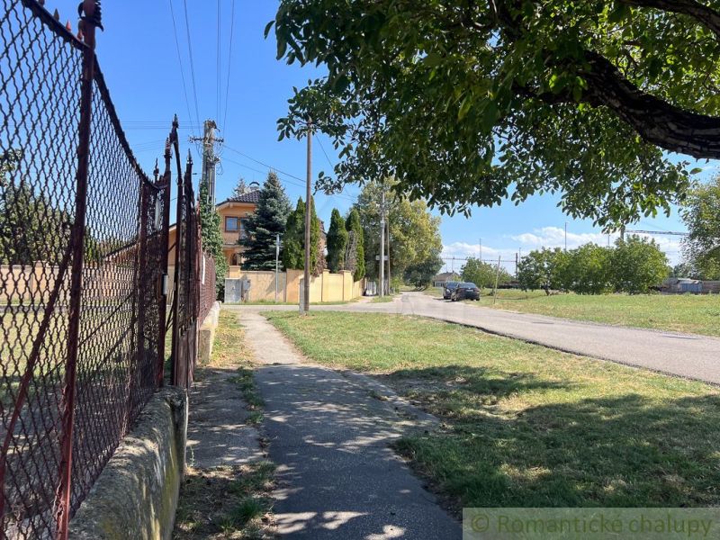 Veľký pozemok na výstavbu v centre Bernolákova. - Chodník vedie popri plote v záhradách Bernolákova, s cestou na pozadí.