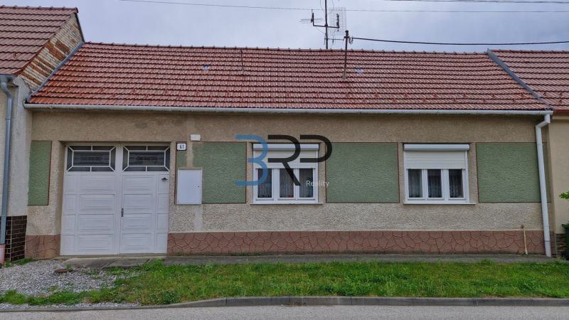 Mokrý Háj - predaj dom - Rodinný dom v Mokrém Háji s červenou strechou a garážovými dverami.