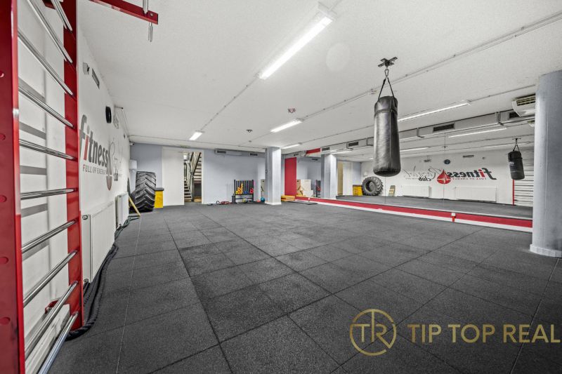 Na predaj PRIESTRANNÉ FITNESS CENTRUM na LUKRATÍVNEJ ADRESE RUŽINOVA - Fitness priestor s boxovacím vrecom, veľkými zrkadlami a čiernou podlahou.