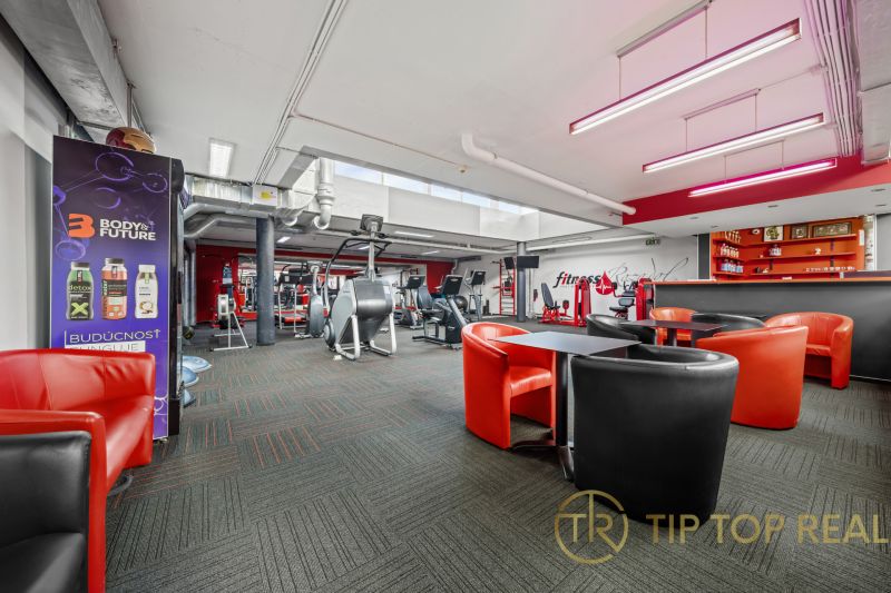 Na predaj PRIESTRANNÉ FITNESS CENTRUM na LUKRATÍVNEJ ADRESE RUŽINOVA - Obchodné priestory s posilňovacími strojmi a červenými koženými kreslami.