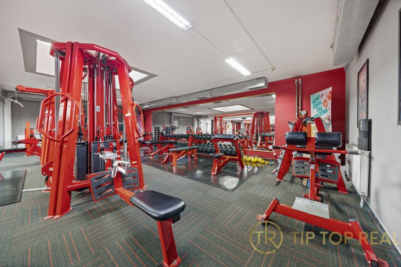 Na predaj PRIESTRANNÉ FITNESS CENTRUM na LUKRATÍVNEJ ADRESE RUŽINOVA - Fitness centrum s červenými posilňovacími strojmi a činkami, obchodné priestory.