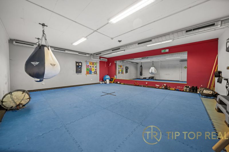 Na predaj PRIESTRANNÉ FITNESS CENTRUM na LUKRATÍVNEJ ADRESE RUŽINOVA - Tréningová miestnosť s vrecom, zrkadlami a modrou žinenkou na podlahe s dreveným dekorom.