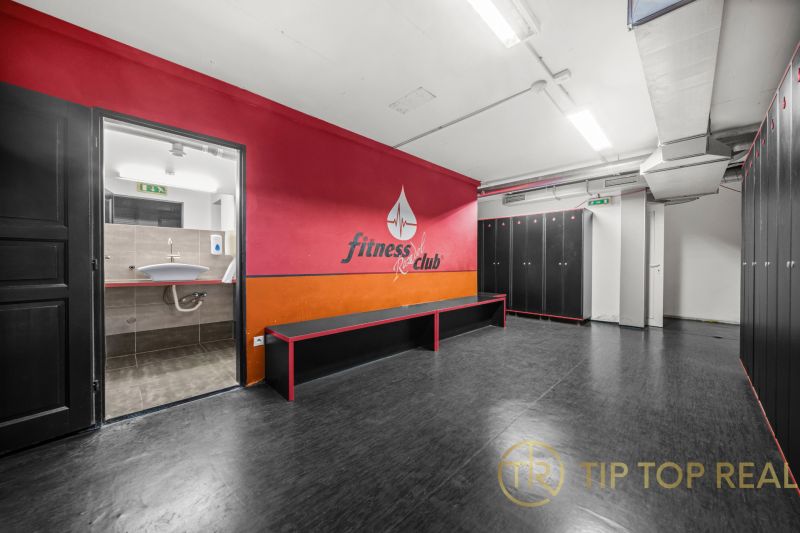 Na predaj PRIESTRANNÉ FITNESS CENTRUM na LUKRATÍVNEJ ADRESE RUŽINOVA - Šatňa s čiernymi skrinkami, lavicou a vstupom do kúpeľne v obchodných priestoroch.