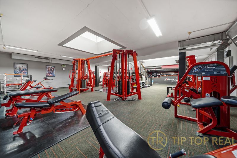 Na predaj PRIESTRANNÉ FITNESS CENTRUM na LUKRATÍVNEJ ADRESE RUŽINOVA - Fitness centrum s posilňovacími strojmi a červenými lavičkami, vhodné obchodné priestory.