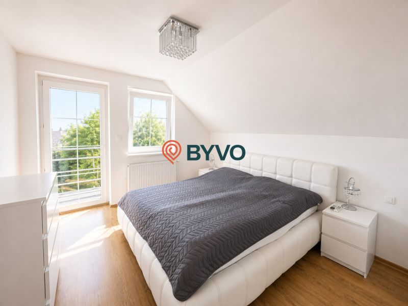 6-izbový rodinný dom v Šamoríne | 201 m² | pozemok 451 m² | - Spálňa v rodinnom dome s veľkým oknom a podlahou s dreveným dekorom.