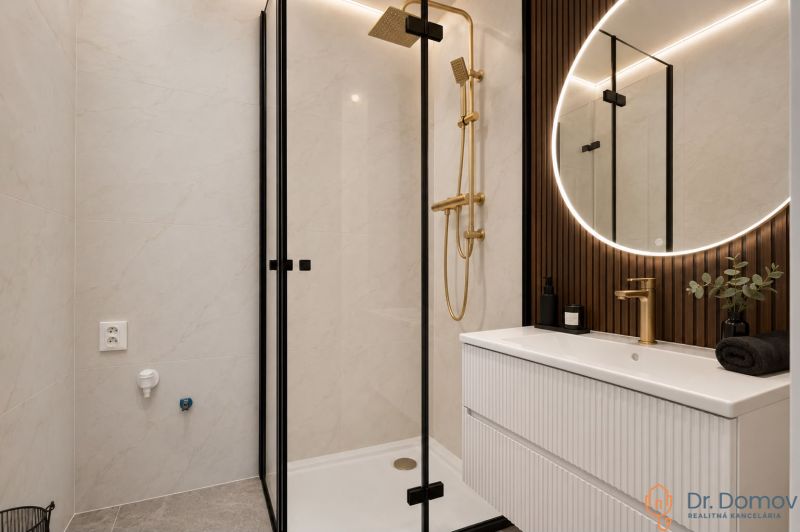 NA PREDAJ ŠTÝLOVÝ A VEĽKÝ 3-IZBOVÝ BYT, KOMPLETNÁ REK., LAMAČ - BA - Kúpeľňa v 3-izbovom byte s elegantnou sprchou, zlatými detailmi a osvetleným zrkadlom.