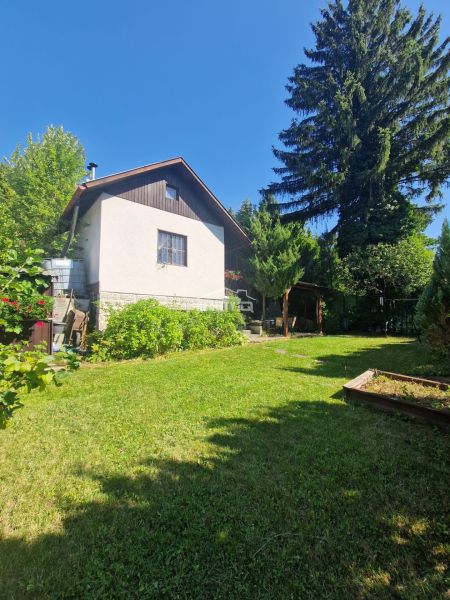 Kúzelná murovaná chata s veľkým altánkom a krbom, predaj Mojšová Lúčka - Záhrada chaty v Žiline s trávnikom a vysokými stromami na pozadí.