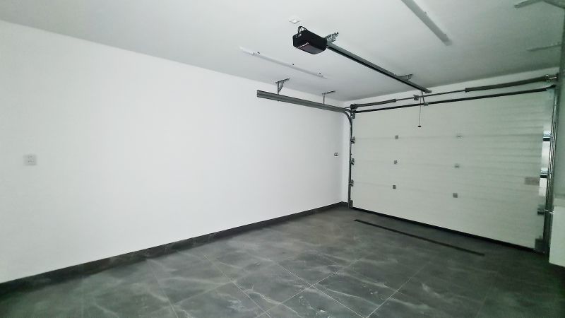 / Novostavba, moderný bungalov, dokončený na kľúč  - Garáž v rodinnom dome s dlažbou, automatickou bránou a svetlými stenami.