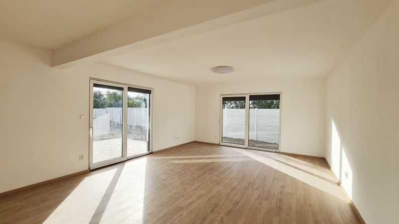 / Novostavba, moderný bungalov, dokončený na kľúč  - Obývačka rodinného domu s podlahou s dreveným dekorom a veľkými oknami na terasu.