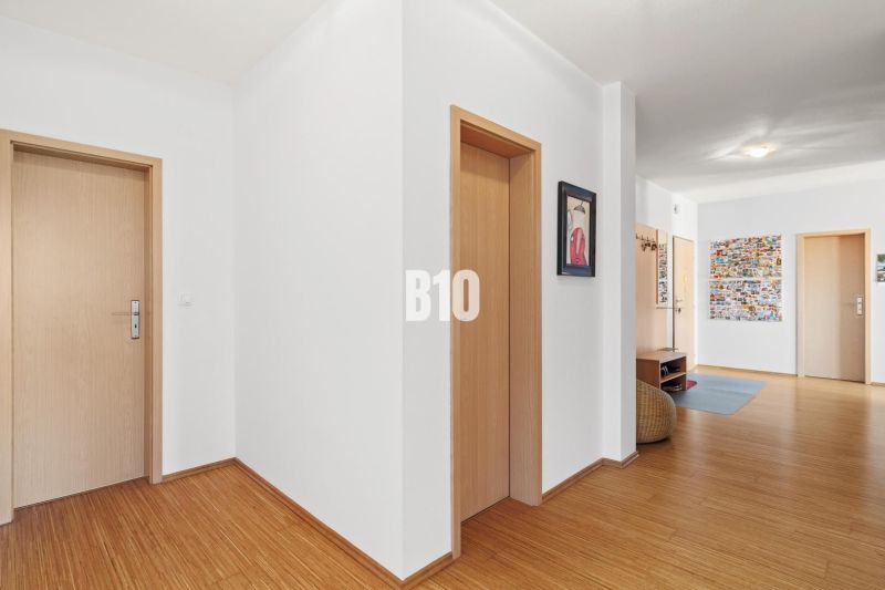 PRIESTRANNÝ 4-IZBOVÝ BYT S DVOMA BALKÓNMI | KRAMÁRE – ul. UHROVA - Chodba v 4-izbovom byte s podlahou s dreveným dekorom a svetlými stenami.