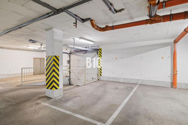 PRIESTRANNÝ 4-IZBOVÝ BYT S DVOMA BALKÓNMI | KRAMÁRE – ul. UHROVA - Podzemné parkovacie státie v 4-izbovom byte so žltými bezpečnostnými pruhmi a potrubiami.