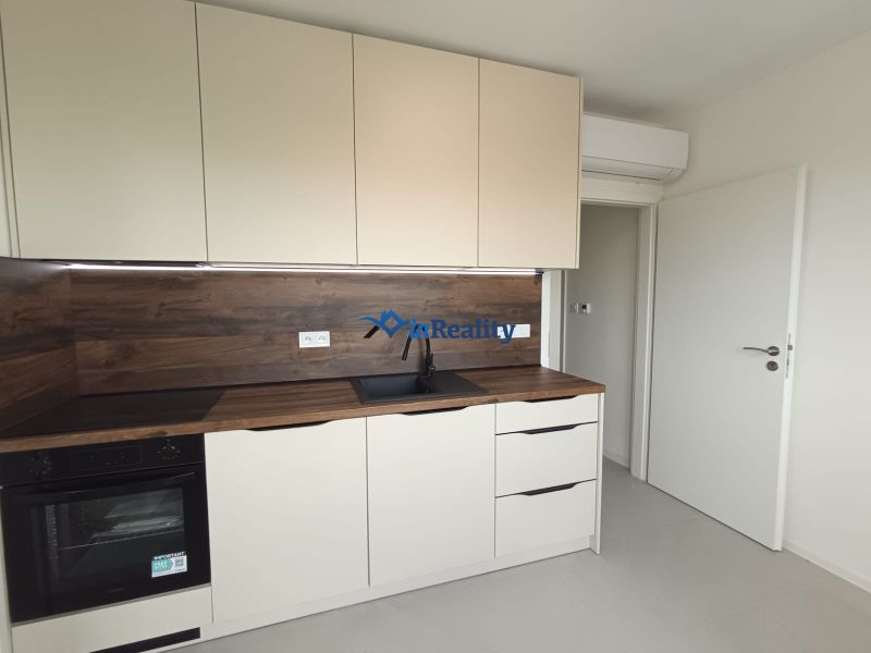 ? Na prenájom: moderný 2 izbový byt – Residence Majakovského, Lučenec - Kuchyňa v 2-izbovom byte s bielymi skrinkami a podlahou s dreveným dekorom.