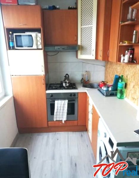1- izbový byt - Košice - Juh, Ostravská ulica - Kuchyňa v 1-izbovom byte s podlahou s dreveným dekorom, základnými spotrebičmi a skrinkami.