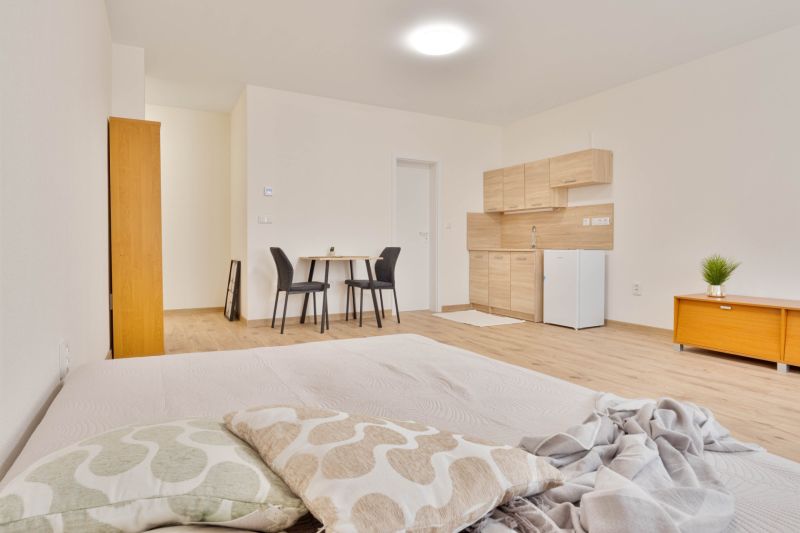 MINÚTU OD NÁMESTIA - VEĽKÁ GARSÓNKA V CENTRE - Garsónka s podlahou s dreveným dekorom, kuchynská linka, jedálenský stôl pre dvoch.