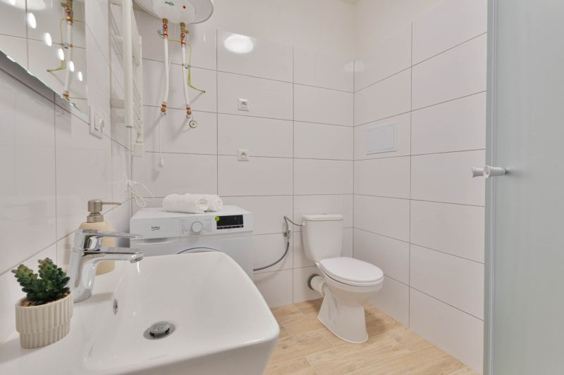 MINÚTU OD NÁMESTIA - VEĽKÁ GARSÓNKA V CENTRE - Kúpeľňa v garsónke s práčkou, umývadlom, toaletou a sprchovým kútom, podlaha s dreveným dekorom.