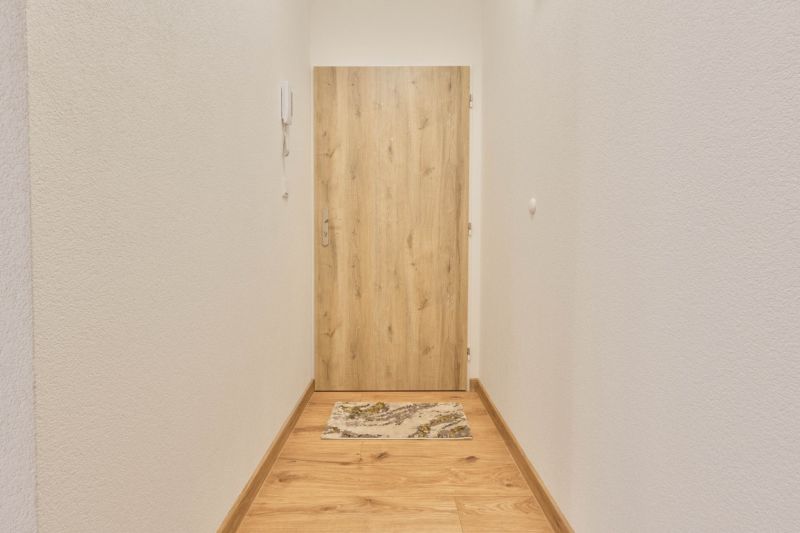 MINÚTU OD NÁMESTIA - VEĽKÁ GARSÓNKA V CENTRE - Úzka chodba s bielymi stenami a dverami s dreveným dekorom v garsónke.