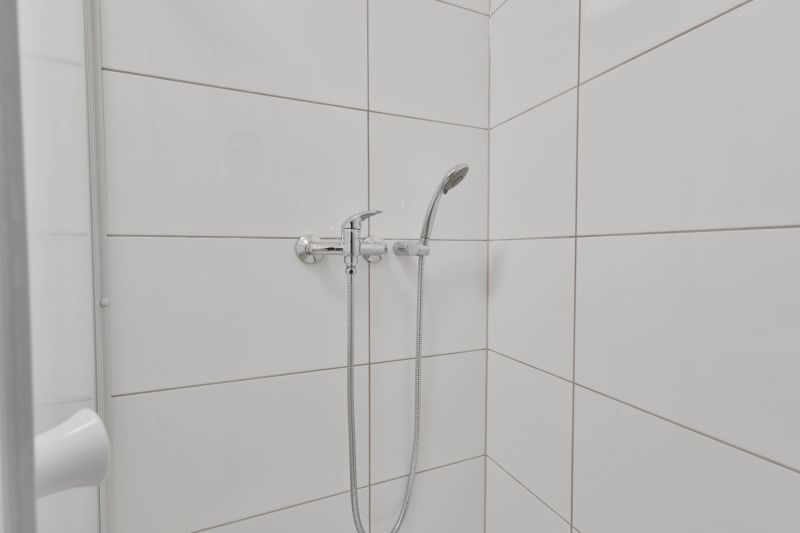 NOVÁ GARSÓNKA V CENTRE - MINÚTU OD NÁMESTIA - Sprchový kút s bielymi obkladačkami a sprchovou hlavicou v garsónke.