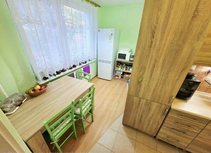 4 izbový byt Bánovce nad Bebravou /CENTRUM - STRED / 80 m2/ PIVNICA - Kuchyňa v 4-izbovom byte so stolom, zelenými stoličkami a podlahou s dreveným dekorom.