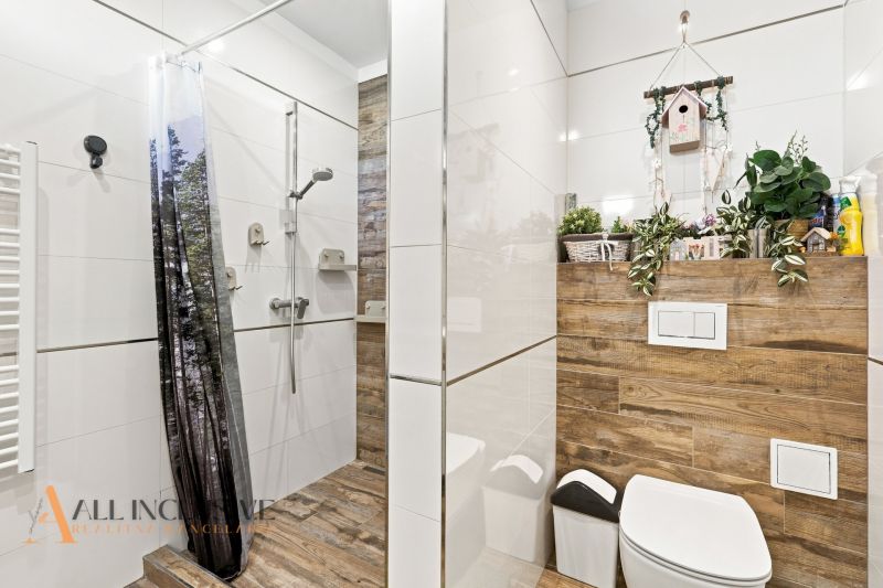 Na predaj moderný 3-izbový radový rodinný dom, Oľdza - Kúpeľňa v rodinnom dome s podlahou s dreveným dekorom a sprchovacím kútom so závesom.