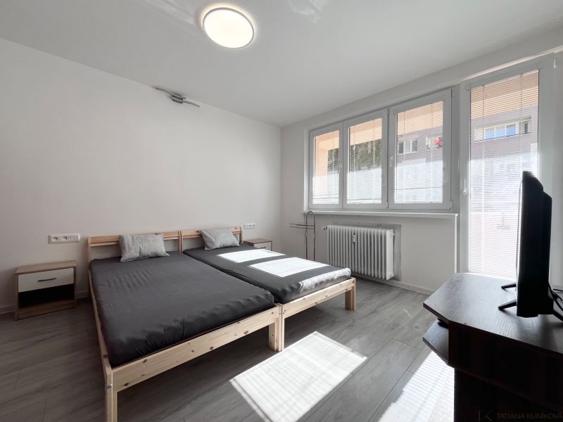 NA PRENÁJOM! Slnečný a zariadený 3i byt 68 m2, ul. Švermova, Trenčín - Svetlá spálňa s posteľou, TV a podlahou s dreveným dekorom v 3-izbovom byte.