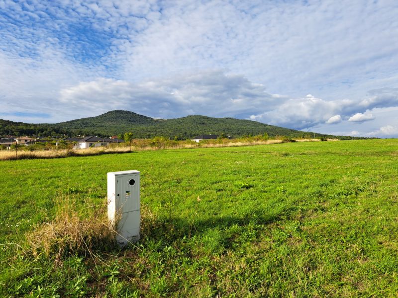 Stavebný pozemok 673 m2 v Štitároch s výhľadom na Zobor i Žibricu - Zelená lúka s domami a kopcom v pozadí v Štitároch, Pozemky - bývanie.
