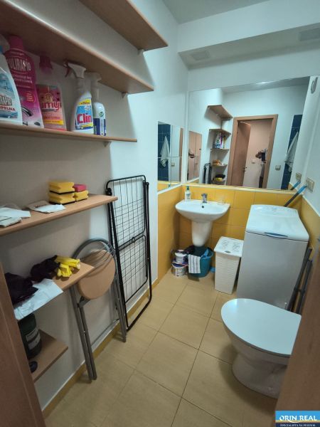KOMPLET ZARIADENÁ GARSÓNKA PRI PLAVÁRNI - Kúpeľňa garsónky s poličkami, spotrebičom a toaletou, podlaha s dreveným dekorom.