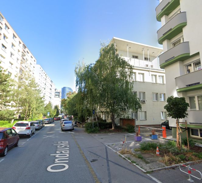 PRENÁJOM-  park. státie na Ondavskej ul. blízko zim. štadióna, BA II - Mestská ulica Ondavská 5 s parkovaním a zeleňou, v pozadí vysoká budova.